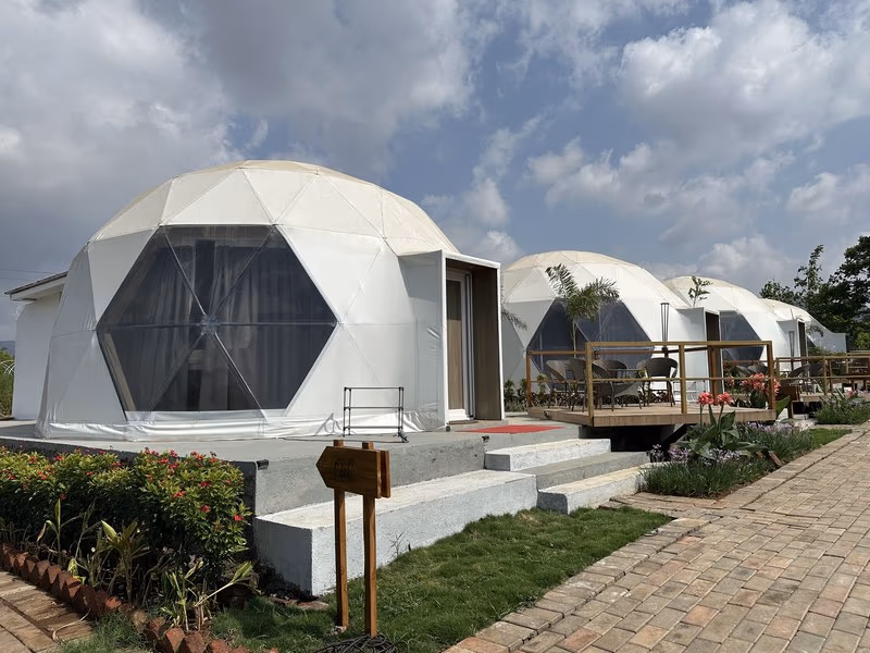 Row of white geodesic glamping domes with glass fronts and wooden decks at The Glen Woods Resort in the Pavana hills